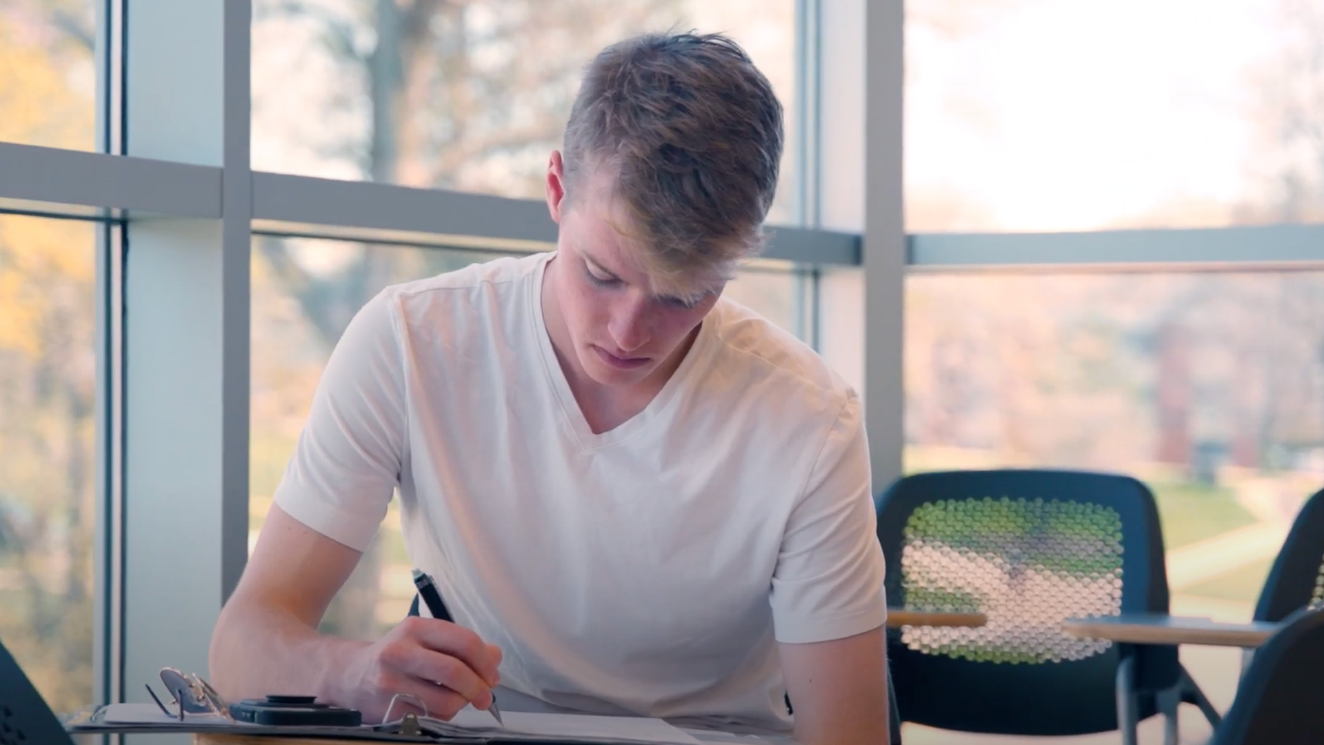 A male student sitting in a classroom taking notes.